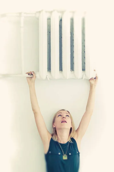 Heating season, high cost of heating concept. A woman holds onto the radiator.