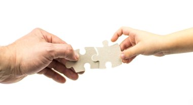 Beyaz arka planda bulmacaları olan bir yetişkinin ve çocuğun eli. İzole edilmiş. Çocukla karşılıklı anlayış kavramı.