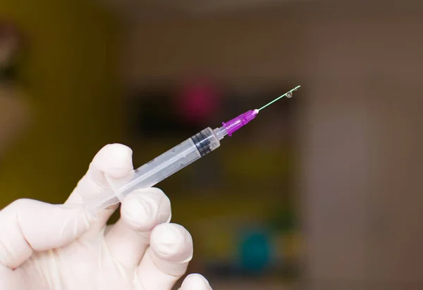 A hand in a white rubber glove holds a syringe on a dark background.