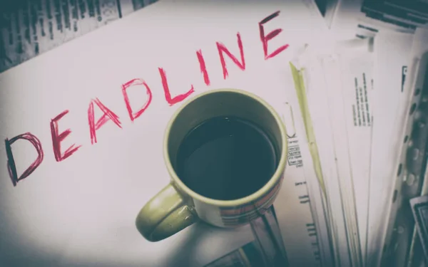 Deadline written on paper and a cup of coffee on scattered papers.