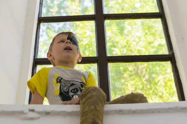 Pencerenin Kenarında Oturan Boyalı Yüzlü Küçük Bir Çocuk — Stok fotoğraf