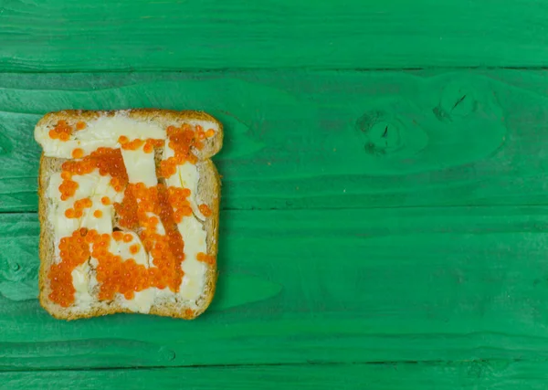 Açık yeşil ahşap zemin üzerinde kırmızı havyarlı iki sandviç..