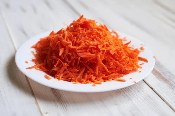 stock image Grated carrots on a plate on a light wooden background.