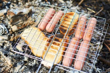 Piknikteki şenlik ateşinin üstünde ızgaradaki sosisler..