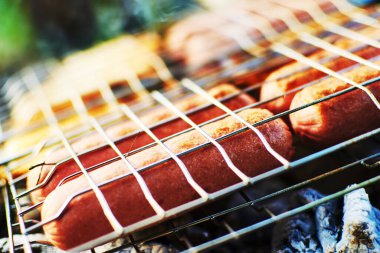 Piknikteki şenlik ateşinin üstünde ızgaradaki sosisler..