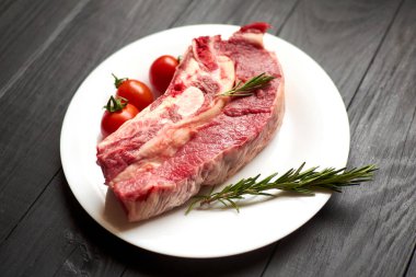 Siyah ahşap arka planda beyaz tabakta çiğ biftek..