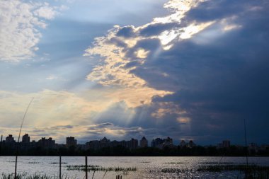 Nehrin ve şehrin üzerindeki kara bulutların arasından güneş ışınları süzülüyor..