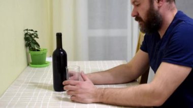 Tıraşsız bir adam kendine şarap koyar. Evde alkolizm, depresyon.