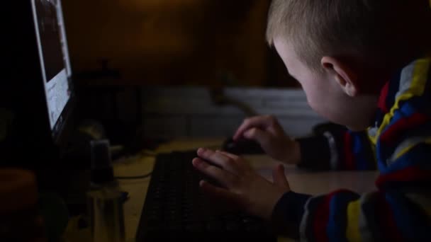 Le petit garçon tape sur le clavier. L'enfant se livre, joue à l'ordinateur dans une pièce sombre .
