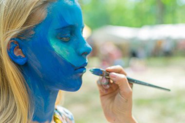 Kızın yüzü tamamen su kiri ile maviye boyanmış. Şenlik hazırlığı.