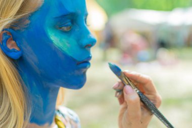 Kızın yüzü tamamen su kiri ile maviye boyanmış. Şenlik hazırlığı.