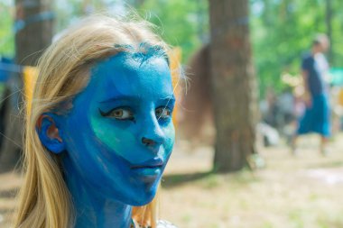 Kızın yüzü tamamen su kiri ile maviye boyanmış. Şenlik hazırlığı.