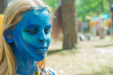 Kızın yüzü tamamen su kiri ile maviye boyanmış. Şenlik hazırlığı.