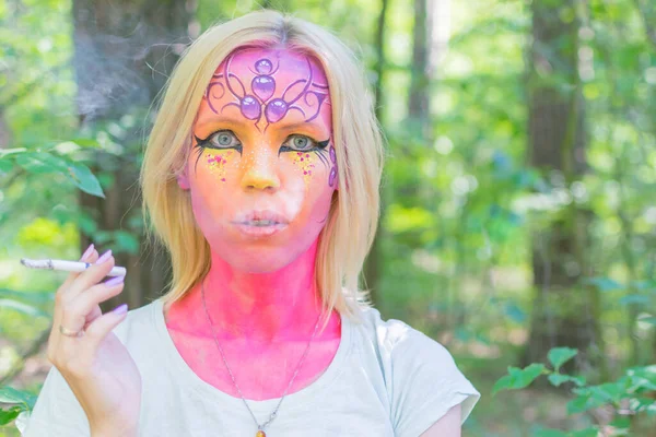 A woman with a painted face smokes. Smoking a fairy creature.