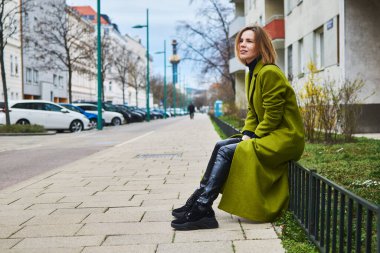 Paltolu bir kadın şehir sokaklarında bir çitin üzerinde dinleniyor..