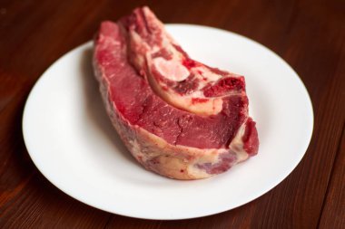 Tahta arka planda beyaz bir tabakta çiğ biftek..