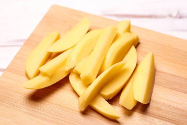 Hafif ahşap arka planda dilimlenmiş patates. Patatesleri pişirmeye hazırlıyorum..