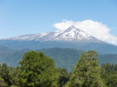 İnanılmaz Choshuenco volkanı bulutlarla çevrili, Panguipulli Gölü 'nün suları üzerinde, ormanın içindeki ağaçlar muhteşem bir volkanik manzara. Güzel, karlı bir zirve. Şili 'nin güneyi. 