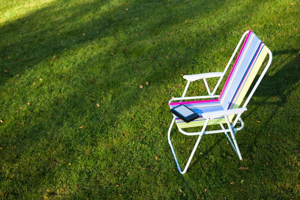 E-Book leitor na cadeira, fundo de grama verde — Fotografia de Stock