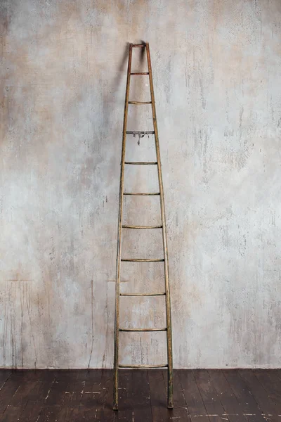 old aged wooden ladder on concrete wall background