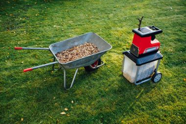 Bahçe neşeli, elektrik shredder (mulcher) ile ahşap malç, yeşil çim arka planını tam el arabası