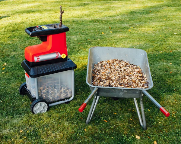 Garden chipper, electric shredder (mulcher) with wheelbarrow full of wooden mulch, green grass background — Stock Photo, Image