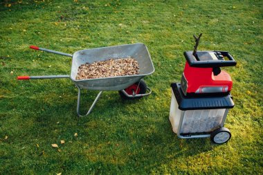 Bahçe neşeli, elektrik shredder (mulcher) ile ahşap malç, yeşil çim arka planını tam el arabası