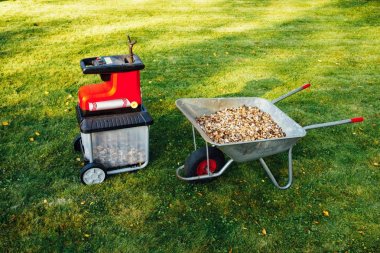 Bahçe neşeli, elektrik shredder (mulcher) ile ahşap malç, yeşil çim arka planını tam el arabası
