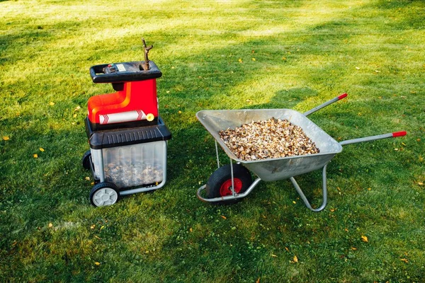 Astilladora de jardín, trituradora eléctrica (mulcher) con carretilla llena de mantillo de madera, fondo de hierba verde —  Fotos de Stock
