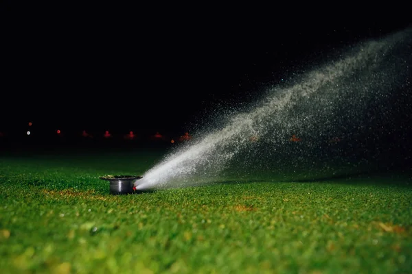 Automatic lawn sprinkler spraying water over golf course green grass at night — Stock Photo, Image