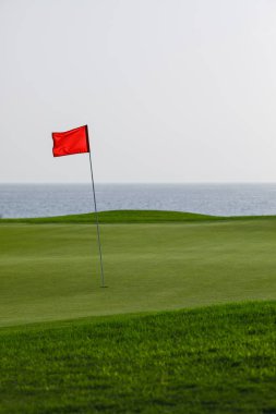 Yeşil çimenler ve kırmızı PIN bayrak, deniz arka plan ile Golf Sahası
