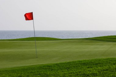 Yeşil çimenler ve kırmızı PIN bayrak, deniz arka plan ile Golf Sahası