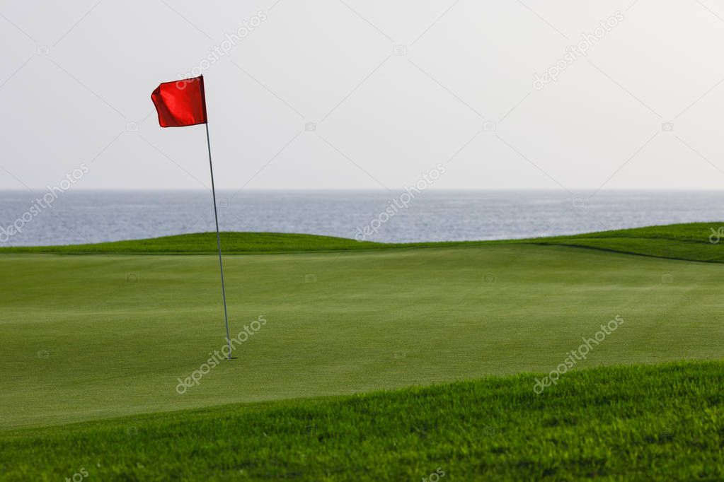golf course with green grass and red pin flag, sea background