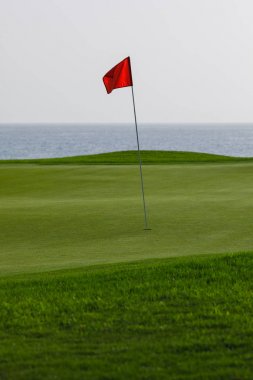 Yeşil çimenler ve kırmızı PIN bayrak, deniz arka plan ile Golf Sahası