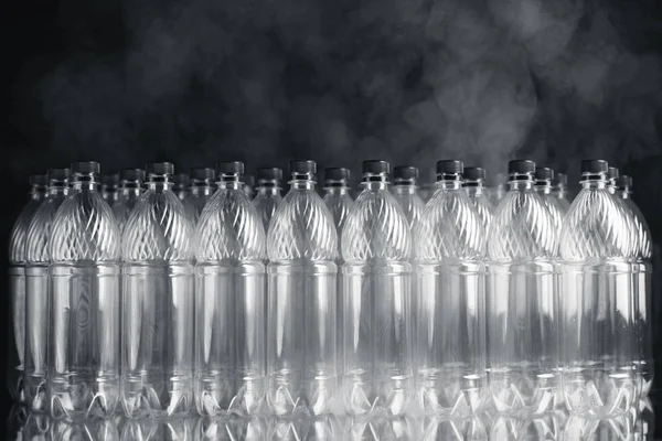 Garrafas de plástico vazias em fundo preto com fumaça, conceito de poluição — Fotografia de Stock