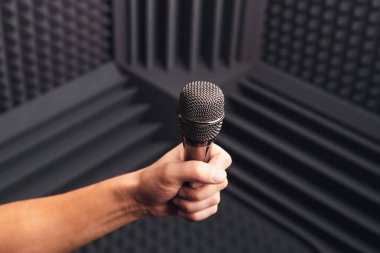 Elinde altın mikrofon, stüdyoda akustik köpükle gri arka plan