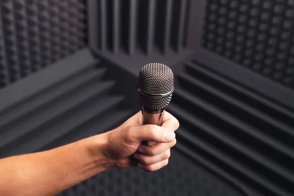 Micrófono dorado en la mano, fondo gris con espuma acústica en el estudio — Foto de Stock