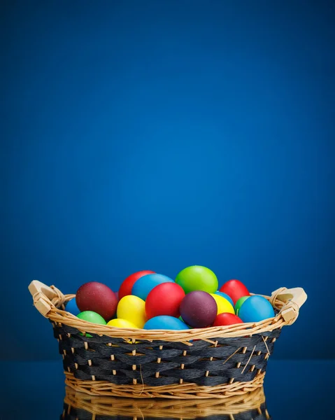 お祝いのギフトバスケットのイースターカラーの卵 コピースペースのある青の背景 — ストック写真