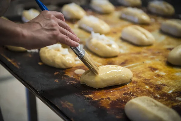 Baker painting buns with beaten egg — Stock Photo, Image