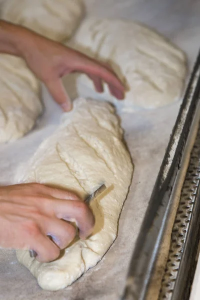 Baker voorbereiden en snijden van ruwe broden te bakken in de oven — Stockfoto