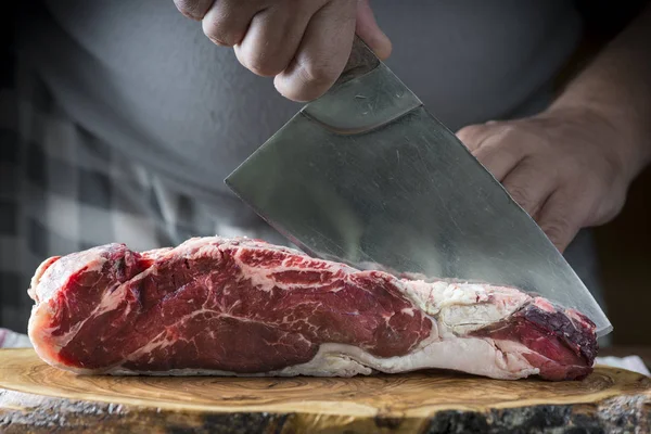 Slaktaren skära en bit kött med en köttyxa — Stockfoto