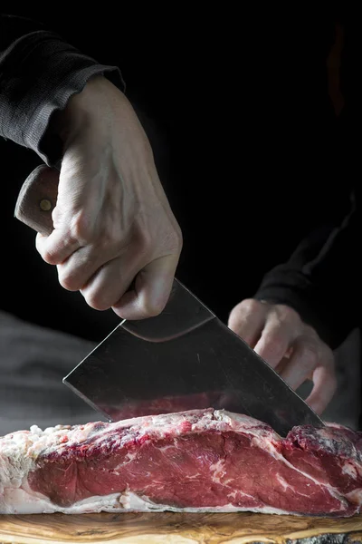 Açougueiro cortando um pedaço de carne com um cutelo — Fotografia de Stock