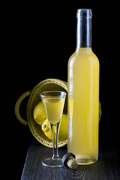 Italian limoncello in a shot glass on a black wooden background — Stock Photo, Image