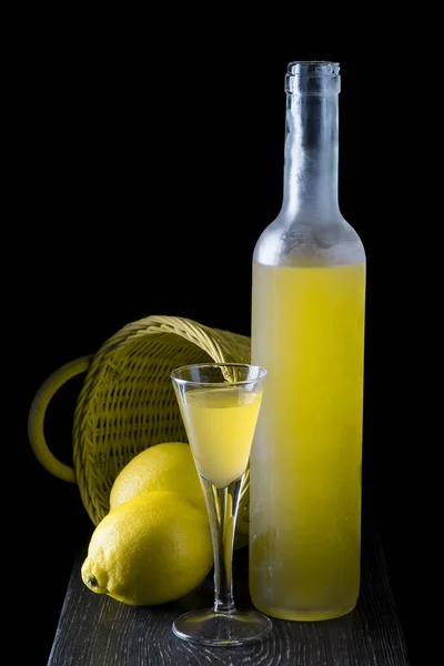 Italian limoncello in a shot glass on a black wooden background — Stock Photo, Image