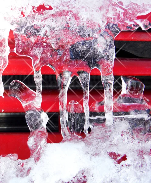 Glänsande klar is istappar hänger på en röd bil yta — Stockfoto