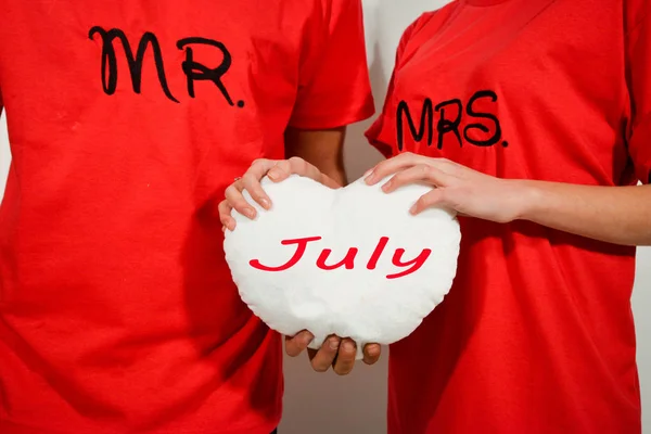 Pareja joven en camisas rojas sosteniendo corazón de tela blanca con texto — Foto de Stock