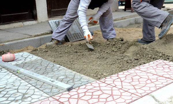 Руки строителя укладывают новые мощеные камни осторожно, располагая их в положении на выровненном и рейковом песчаном основании
