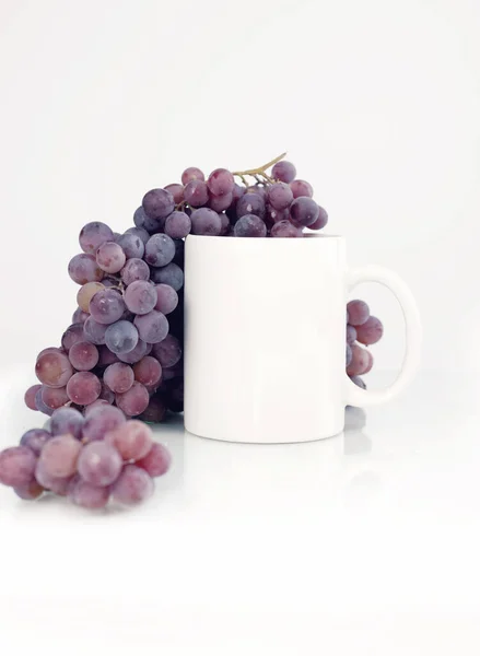 Beyaz kupa, beyaz arka planda mor üzümler. Sonbahar tarzı model.