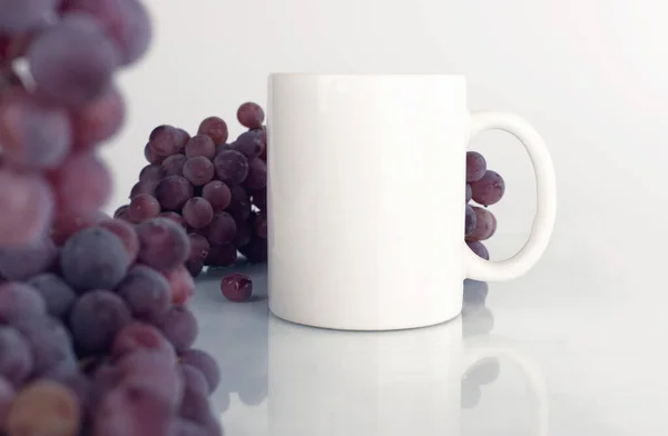 Beyaz kupa, beyaz arka planda mor üzümler. Sonbahar tarzı model.