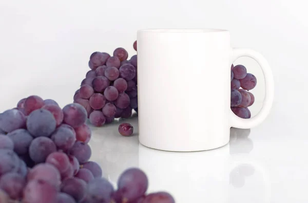 Beyaz kupa, beyaz arka planda mor üzümler. Sonbahar tarzı model.